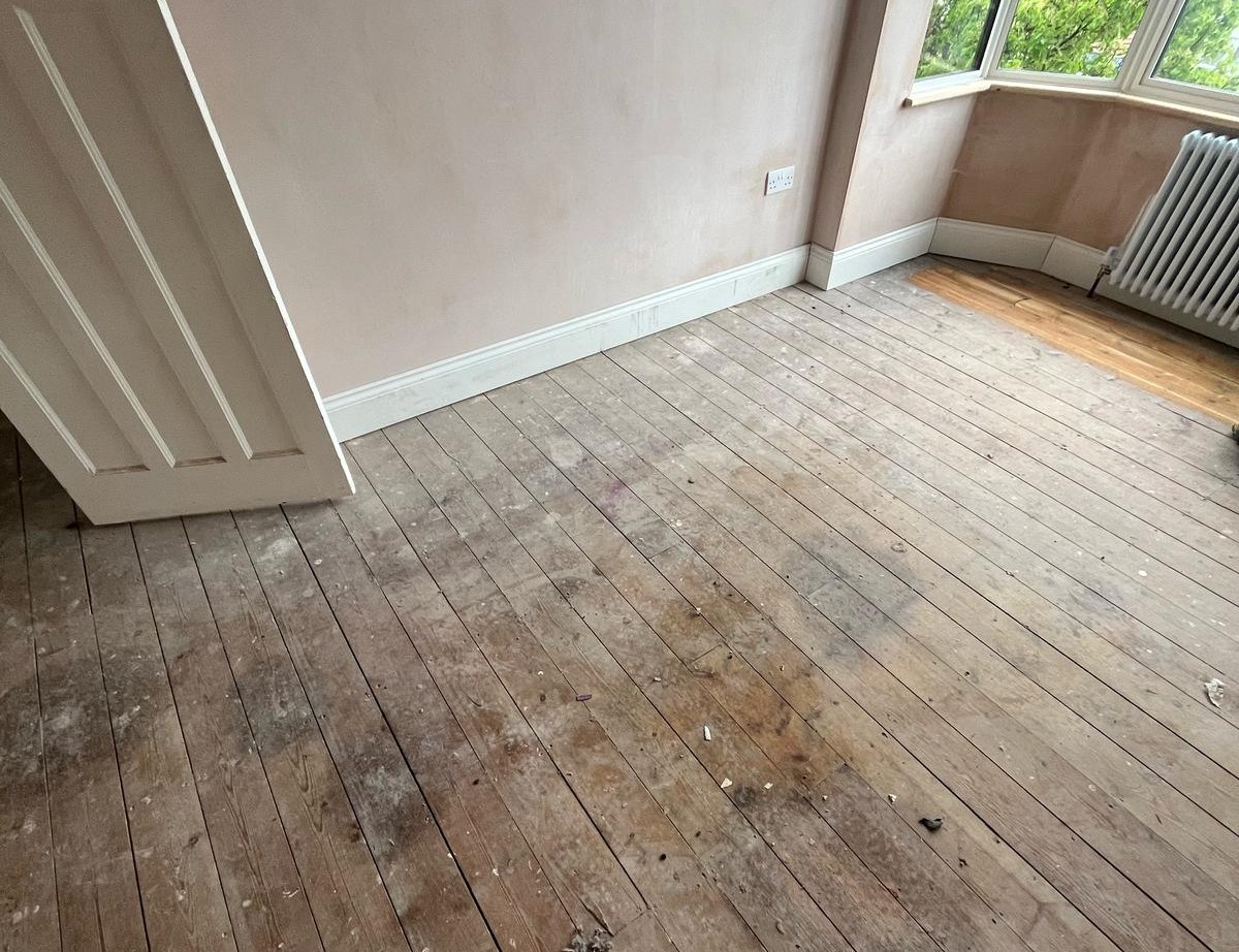 Before restoration view of a bedroom in Southwest London with worn, dusty Victorian pine floorboards (softwood) ready for sanding and staining wood floors.