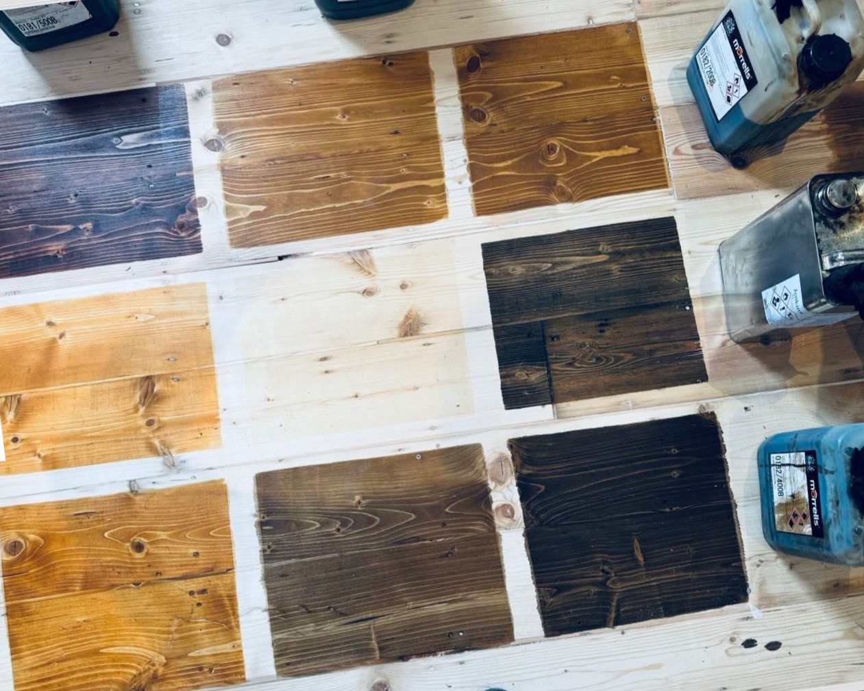 On-floor colour samples for staining wood floors in Southwest London: multiple test patches on sanded Victorian pine floorboards (softwood) with stain containers visible.