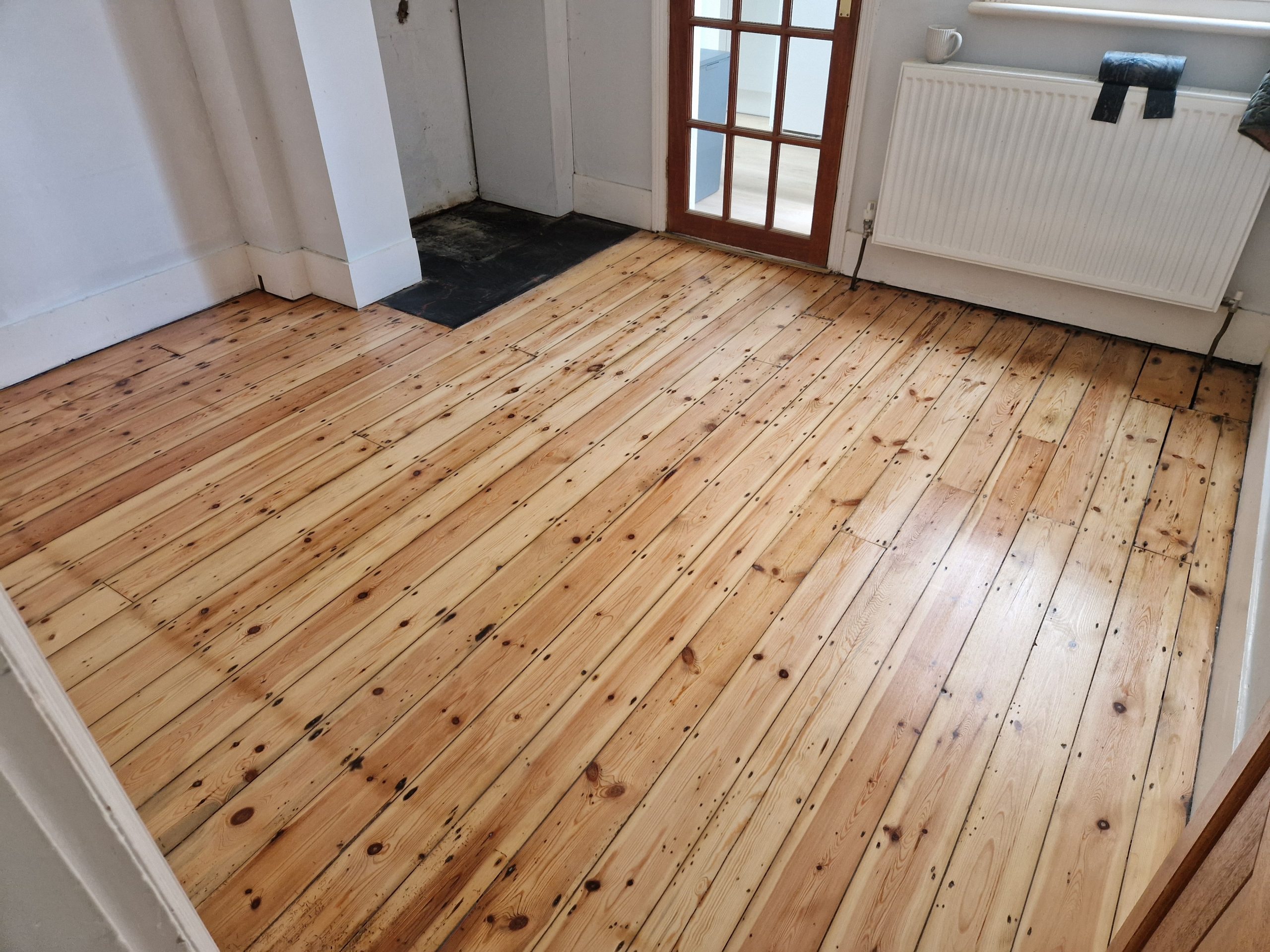 Finished living room in Southwest London with restored Victorian pine floorboards (softwood), showing an even honey tone and satin sheen after staining wood floors.