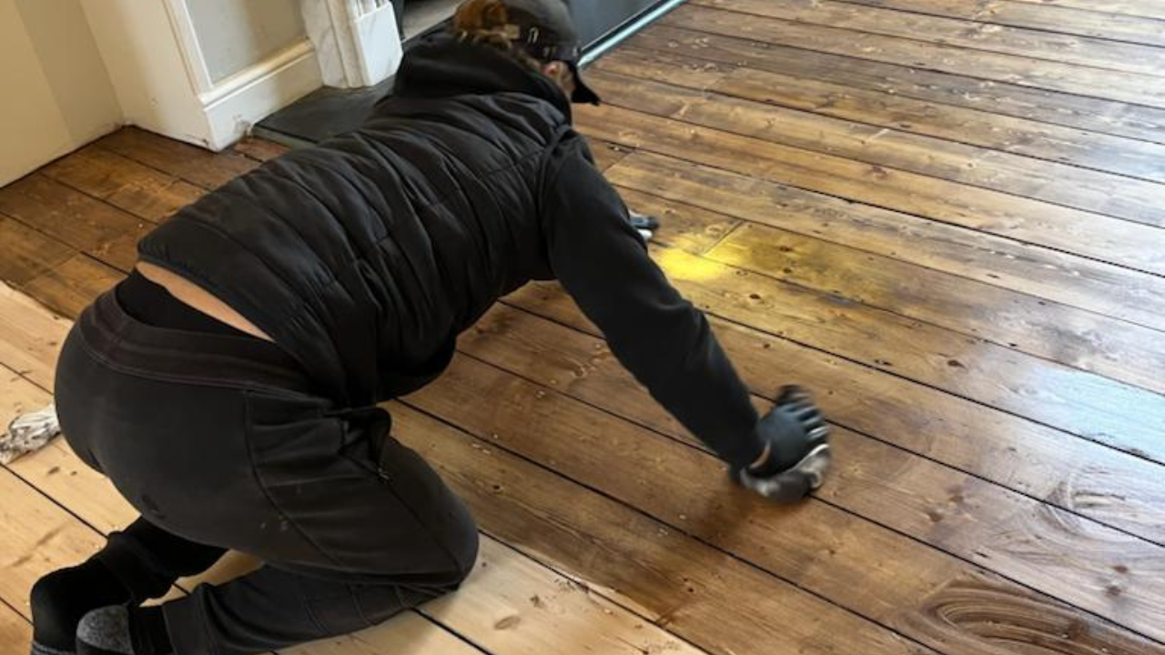 Technician hand-applying stain to Victorian pine floorboards (softwood) in Southwest London, showing half-sanded boards beside darker finished sections during staining wood floors.