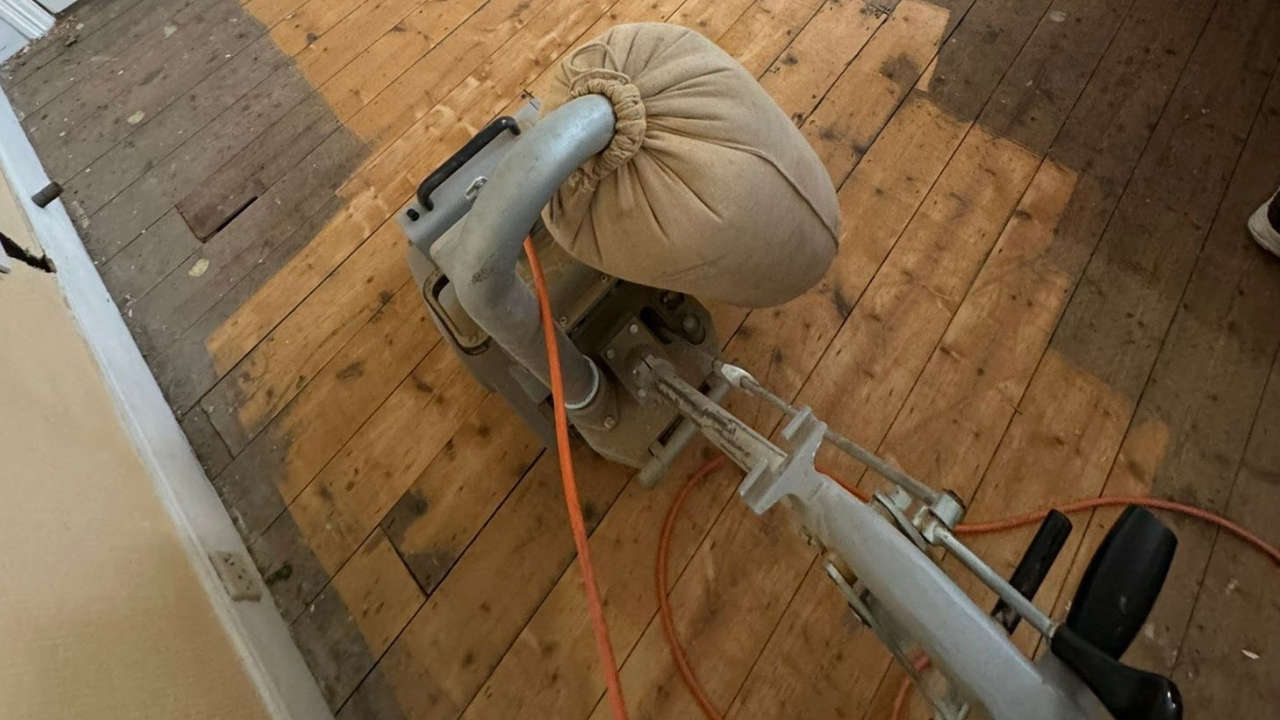 Belt sander mid-pass on Victorian pine floorboards (softwood) in Southwest London, removing old finish and levelling the surface before staining wood floors.