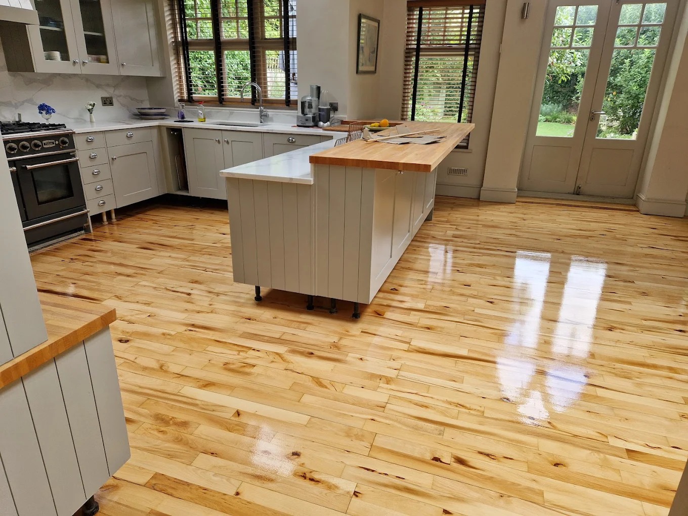 Bright kitchen after Worktop Refinishing in South West London, featuring a restored butcher-block island worktop and glossy maple plank hardwood floor.