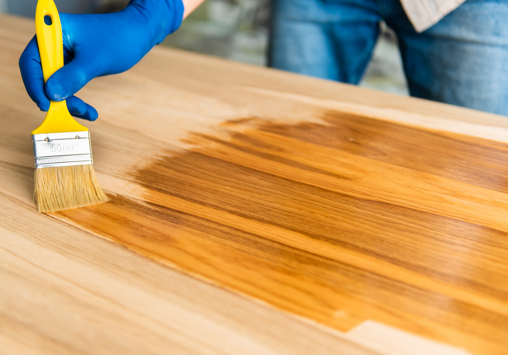 Worktop Refinishing in South West London, with a technician applying finish to a solid oak wooden kitchen worktop above a matching hardwood plank floor.