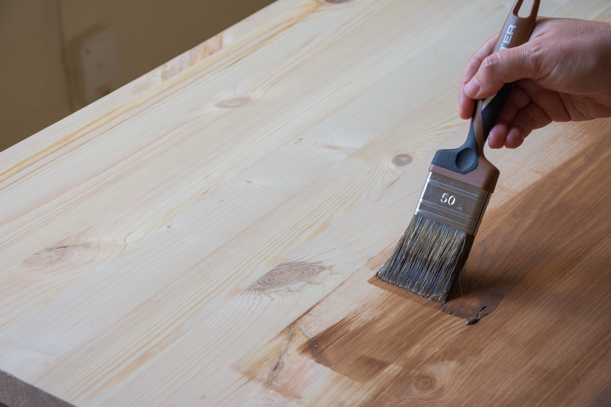 Worktop Refinishing in South West London, with a technician brushing stain onto a solid pine wooden kitchen worktop above matching pine plank floorboards.