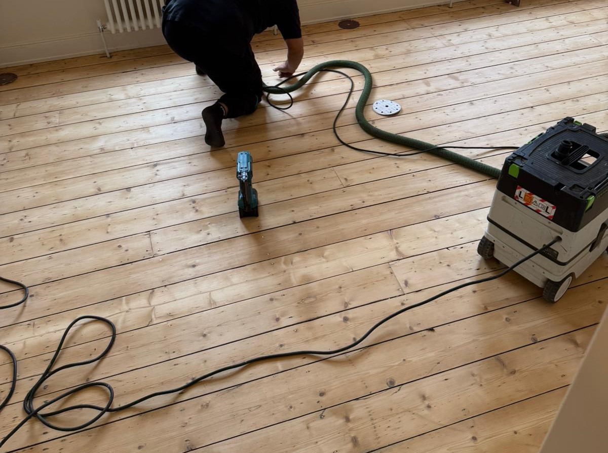 Wood Floor Sanding in South West London bedroom with technician dust-extracting freshly sanded pine softwood floorboards