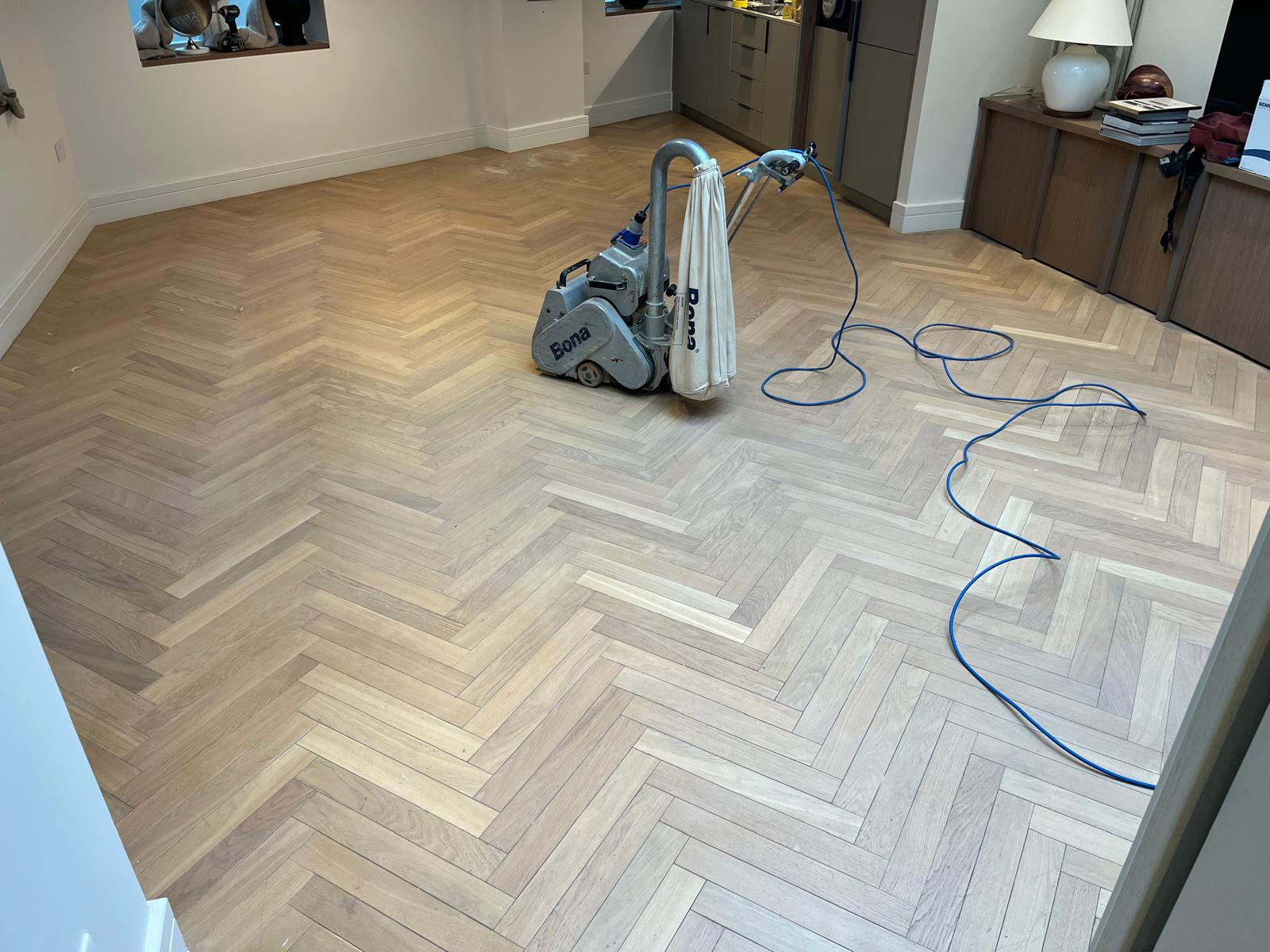 Wood Floor Sanding in south west london living room on light oak herringbone parquet floor with professional Bona belt sander in progress