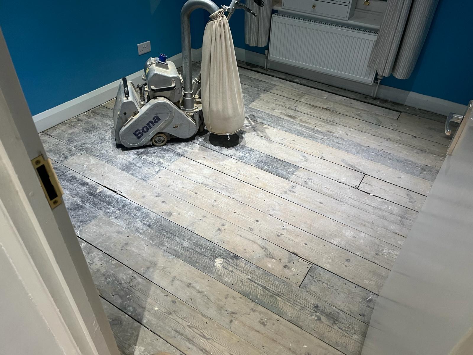 Wood Floor Sanding in south west london bedroom with professional Bona belt sander working on original pine floorboards before refinishing